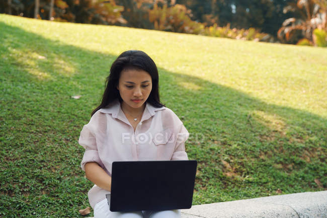 Young asian woman using laptop in park — Stock Photo