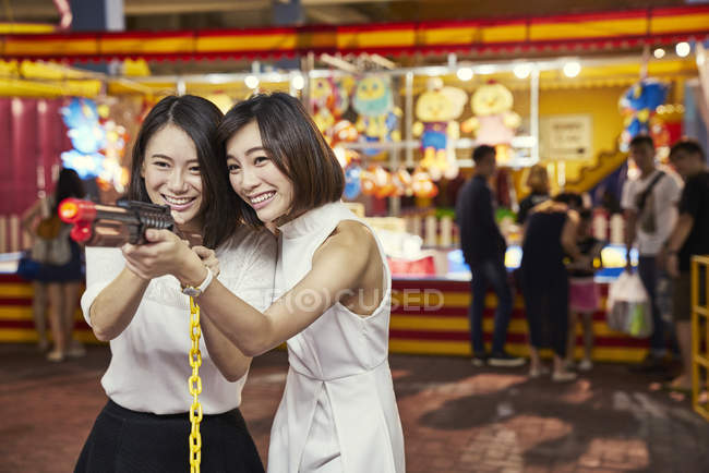 Amigos jugando un juego de disparos en un carnaval para ganar premios en Singapur - foto de stock