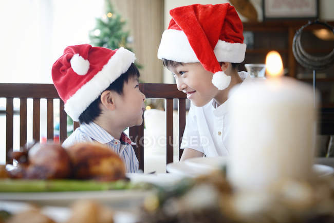 Famiglia asiatica che celebra le vacanze di Natale, due fratelli in cappelli di Babbo Natale a tavola — Foto stock