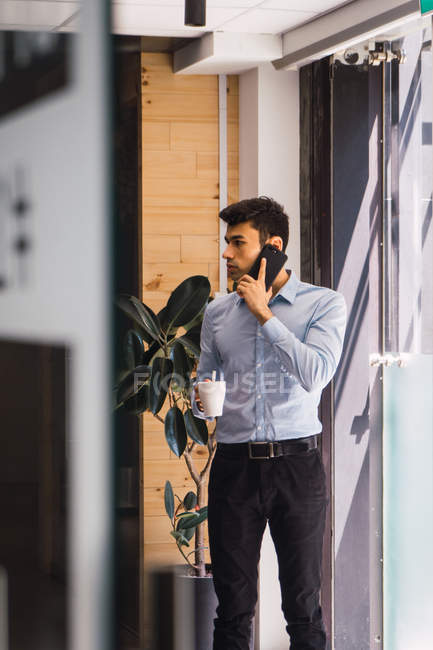 Hombre de negocios adulto joven utilizando el teléfono inteligente en la oficina moderna - foto de stock