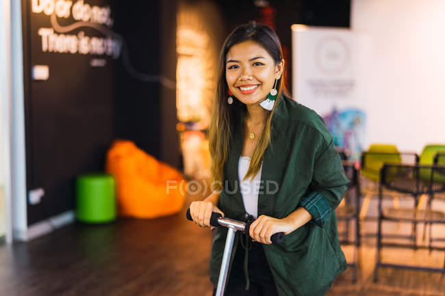 Jeune asiatique femme d'affaires avec scooter dans le bureau moderne — Photo de stock
