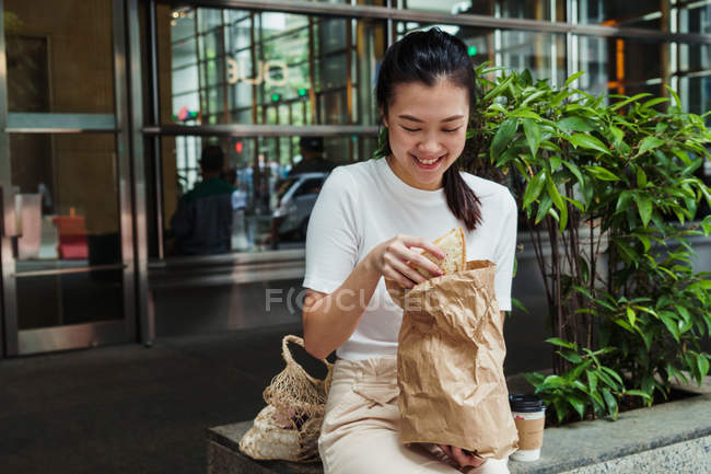 Young attractive asian woman eating sandwich — Stock Photo