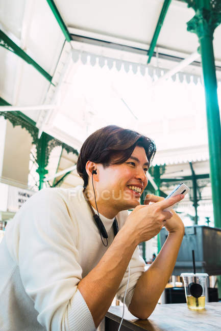 Усміхнений азіатський чоловік використовує смартфон у кафе — стокове фото