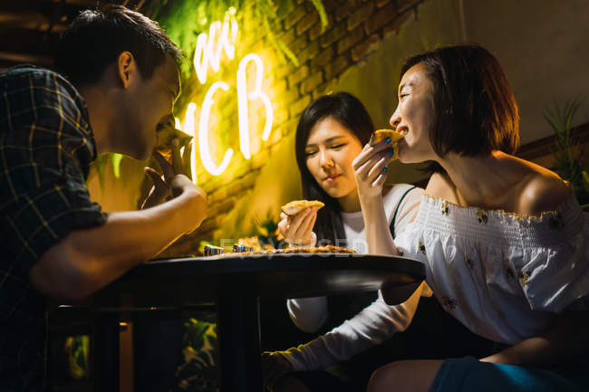 Молоді азіатські друзі їдять піцу в зручному барі — стокове фото