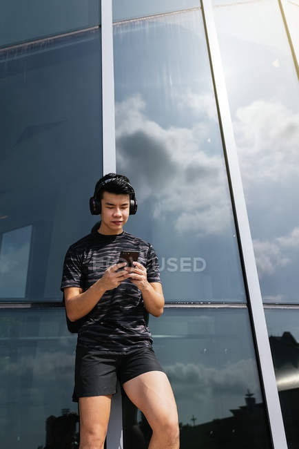 Felice asiatico sportivo uomo utilizzando smartphone e cuffie — Foto stock