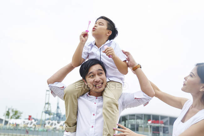 Счастливая азиатская семья вместе, отец давая кататься на спине мальчика с пузырьками — стоковое фото