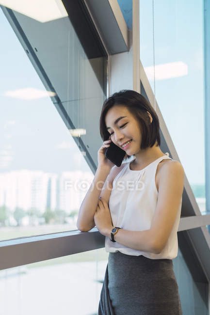 Giovane donna d'affari asiatica che parla su smartphone in ufficio moderno — Foto stock