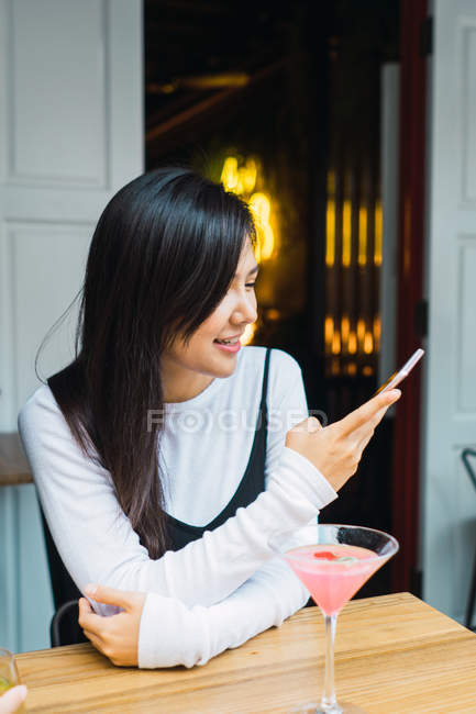 Молодая азиатка со смартфоном в уютном баре — стоковое фото