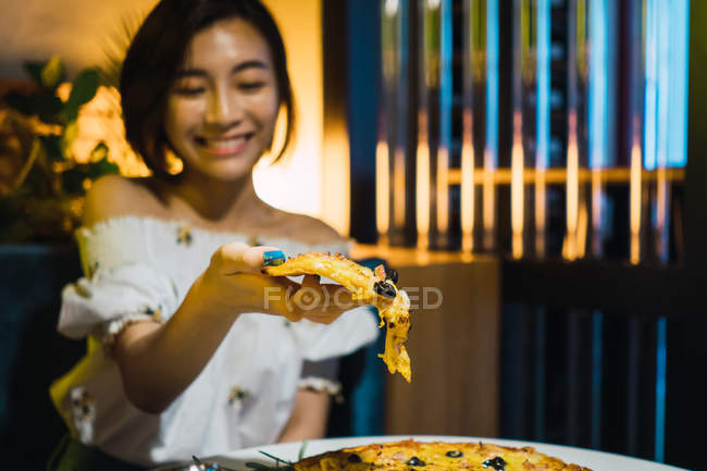 Young asian woman taking slice of pizza in comfortable bar — Stock Photo