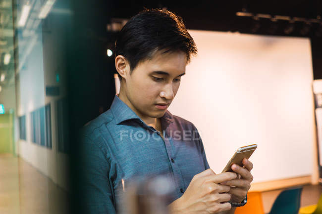 Jovem asiático homem de negócios usando smartphone no escritório moderno — Fotografia de Stock