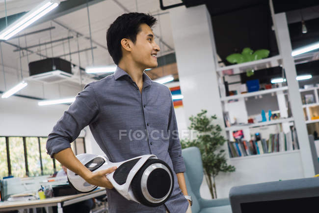 Joven asiático hombre de negocios con hoverboard en moderno oficina - foto de stock
