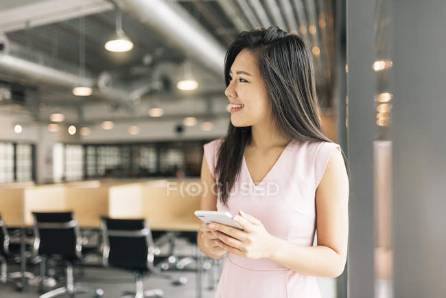Молодая азиатская успешная деловая женщина со смартфоном в современном офисе — стоковое фото