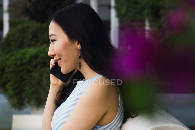 Vista lateral de la joven mujer asiática hablando en smartphone - foto de stock