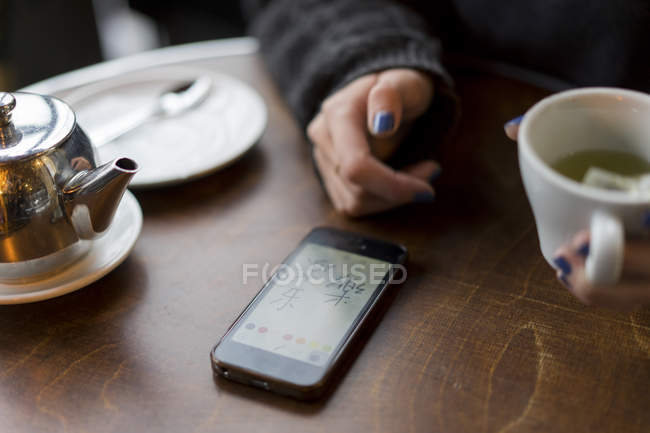 Imagen recortada de la mujer con teléfono inteligente en la cafetería - foto de stock