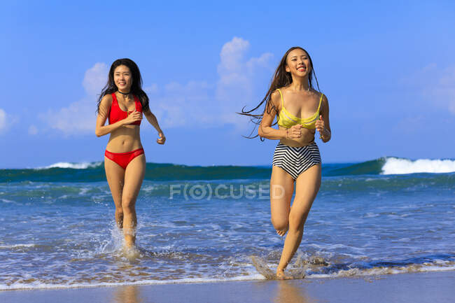Zwei junge asiatische Frauen haben eine großartige Zeit in den Wellen des Ozeans. — Stockfoto