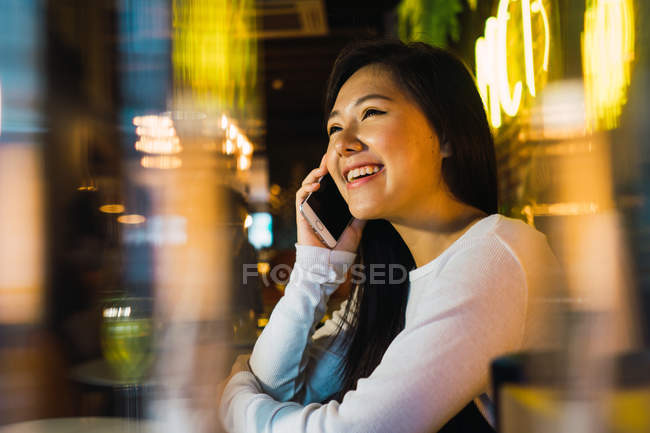 Jeune femme asiatique à l'aide de téléphone portable dans un bar confortable — Photo de stock