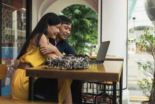 Heureux jeune asiatique couple à l'aide d'ordinateur portable dans café — Photo de stock