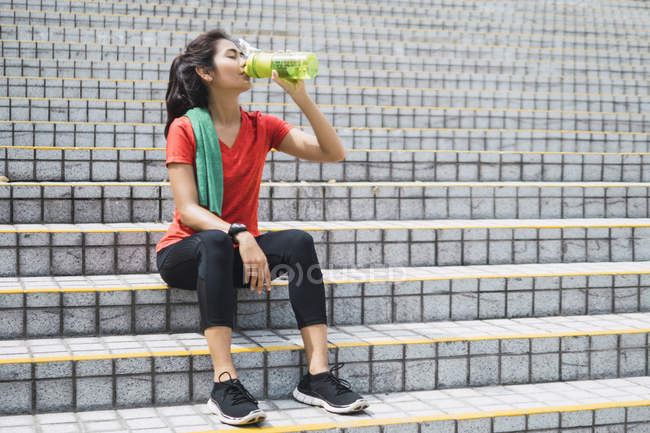 Молодая азиатская спортсменка пьет воду на лестнице — стоковое фото