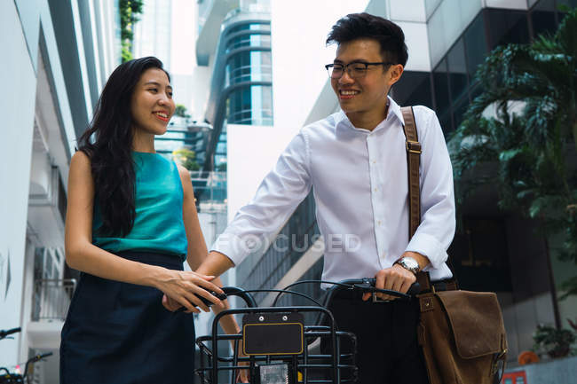 Young adult business couple walking with bicycle — Stock Photo