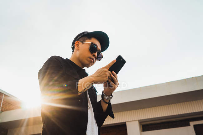 Крутой молодой человек с помощью смартфона на улице — стоковое фото