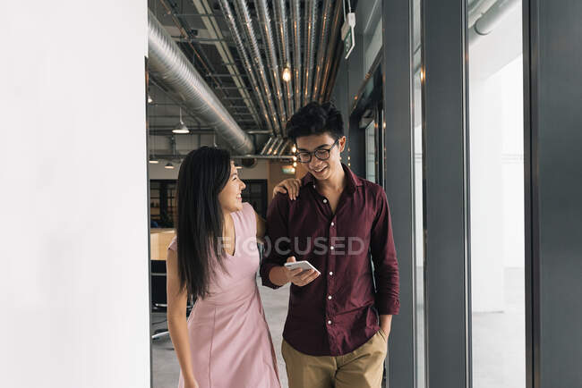 Пара молодых азиатских рабочих со смартфоном в офисе — стоковое фото
