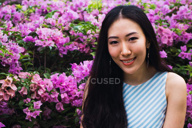 Junge Asiatin posiert gegen Blumen — Stockfoto