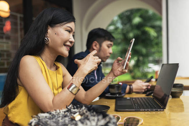Heureux jeune asiatique couple à l'aide de dispositifs numériques dans café — Photo de stock