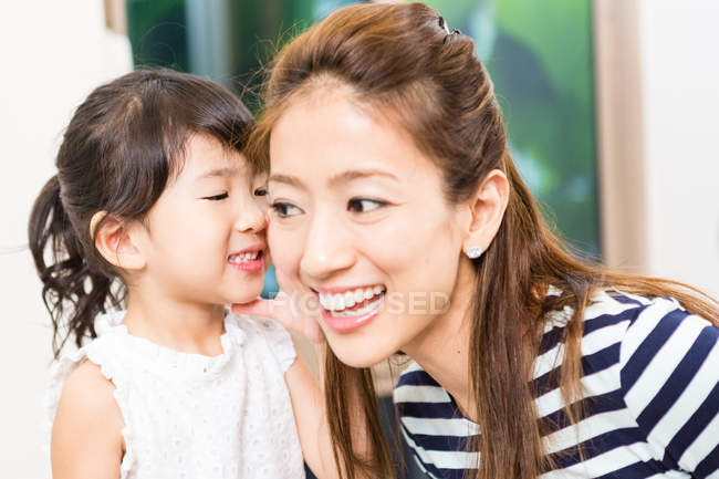 Little girl whispering into mother ear. — Stock Photo