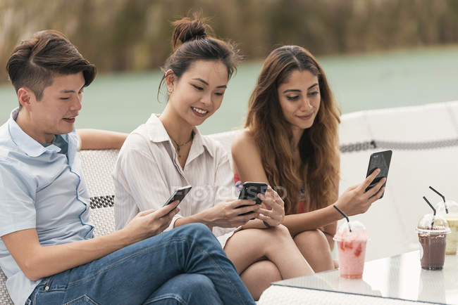 Grupo de amigos en un restaurante, usando sus teléfonos - foto de stock