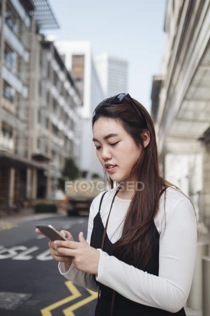 Chinese long hair woman with smartphone against road — Stock Photo
