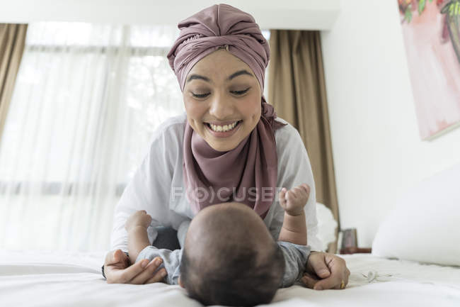 Азіатська мусульманська мати грає з дитиною на ліжку — стокове фото