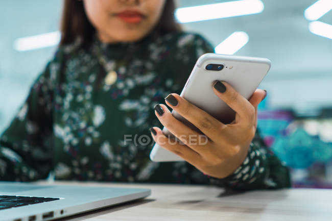 Image recadrée de femme d'affaires asiatique en utilisant smartphone dans le bureau moderne — Photo de stock