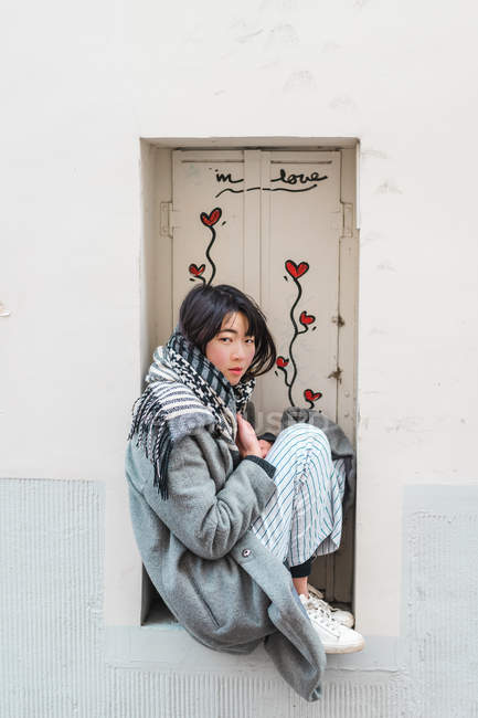 Молодая взрослая азиатка сидит на подоконнике с цветами — стоковое фото