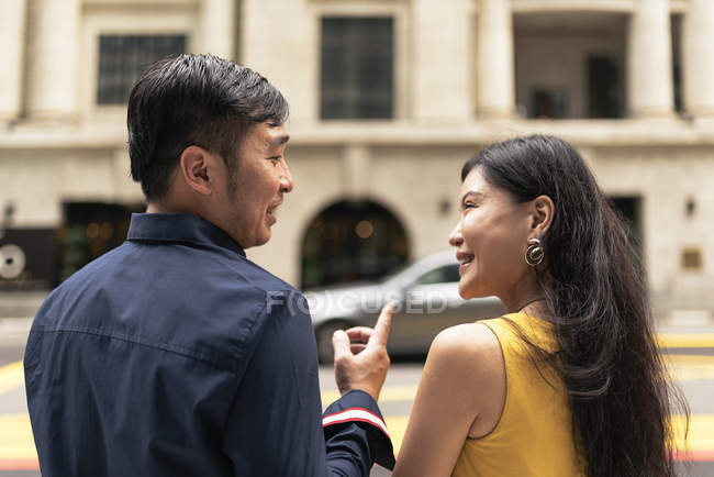 Счастливая молодая азиатская пара, идущая по улице, мужчина указывает на что-то — стоковое фото
