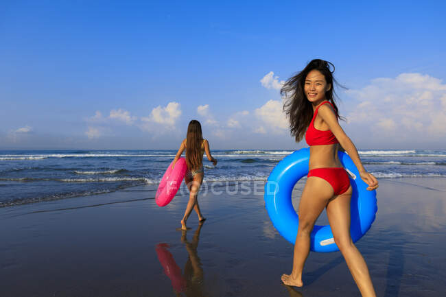 Дві красиві дівчата з флюгерами на шляху до хвиль океану. Одна дівчина обертається навколо посміхаючись . — стокове фото