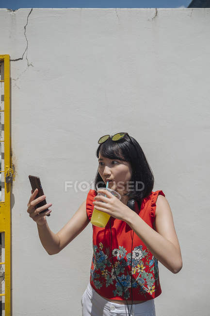 Asian woman with Smartphone against white wall — Stock Photo