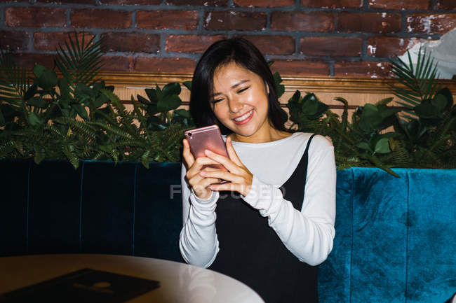 Jovem asiático mulher com smartphone no confortável bar — Fotografia de Stock