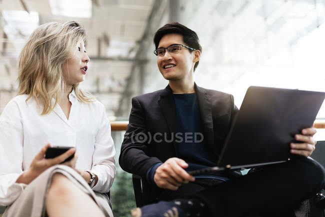 Young asian couple of businesspeople with laptop and smartphone in airport — Stock Photo