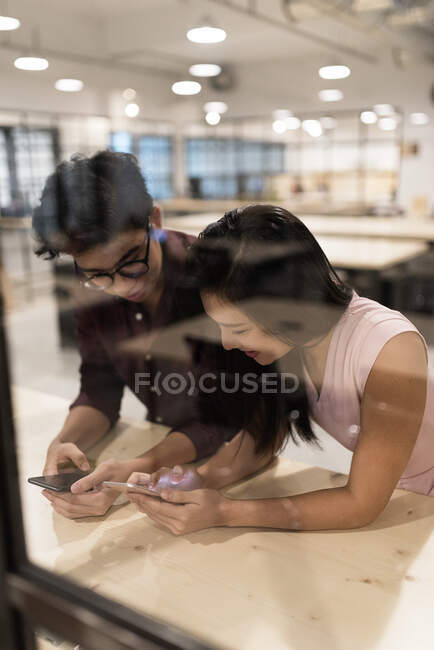 Compañeros asiáticos en la oficina usando teléfonos inteligentes - foto de stock