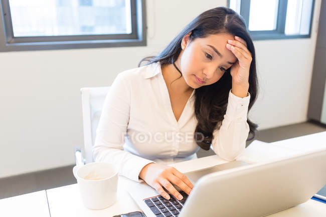 Беспокойная молодая женщина работает на ноутбуке в современном офисе — стоковое фото