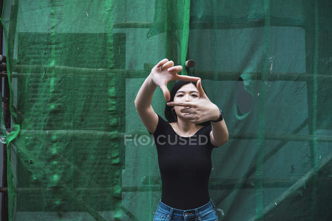 Jeune attrayant asiatique fille montrant cadre par doigts à l'extérieur — Photo de stock