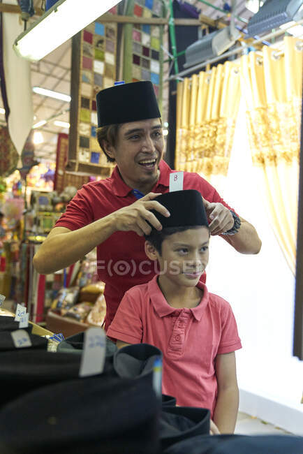Padre e hijo comprando Songkoks en Geylang Hari Raya Bazaar, Singapur - foto de stock