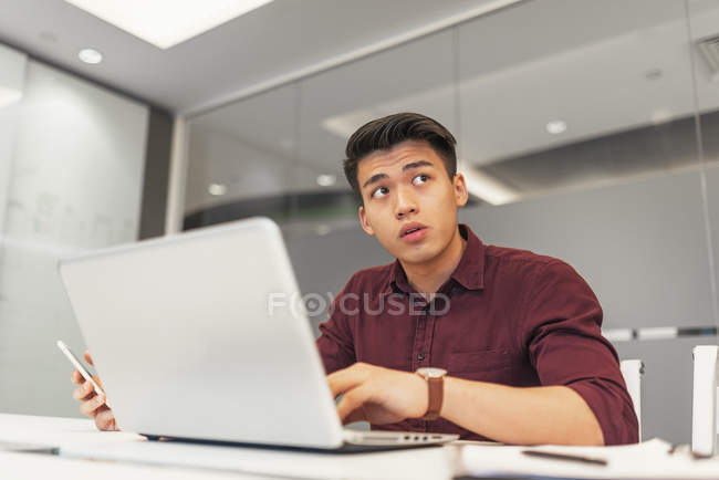 Молодий азіатський бізнесмен використовує ноутбук в сучасному офісі — стокове фото