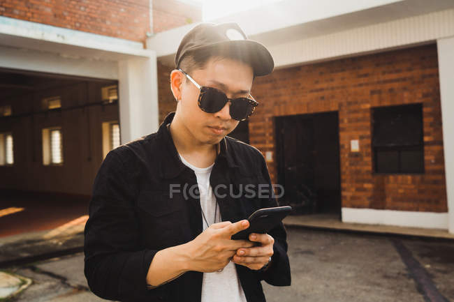 Cool giovane asiatico uomo utilizzando smartphone all'aperto — Foto stock