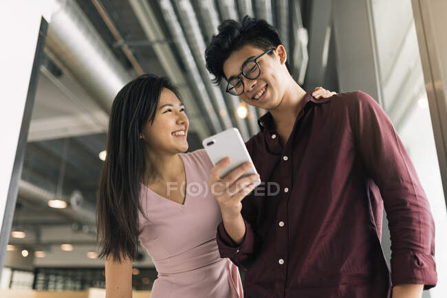 Молода азіатська успішна ділова пара обмінюється смартфонами в сучасному офісі — стокове фото