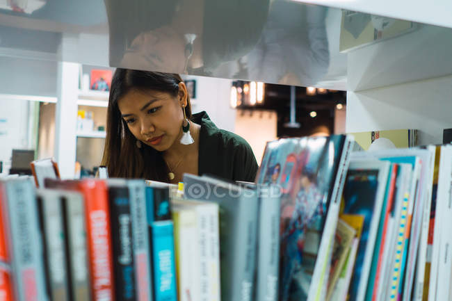 Jeune asiatique femme d'affaires à la recherche de livres dans le bureau moderne — Photo de stock
