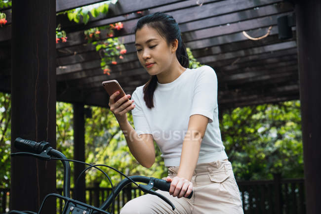 Jeune attrayant asiatique femme avec vélo en utilisant smartphone — Photo de stock