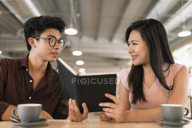 Young asian successful business people with coffee sharing notes in modern office — Stock Photo
