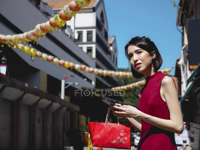 Chinese woman using smartphone and holding purse — Stock Photo