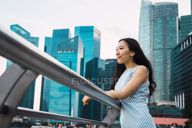 Молода азіатка стоїть на перилах з хмарочосами на фоні — стокове фото